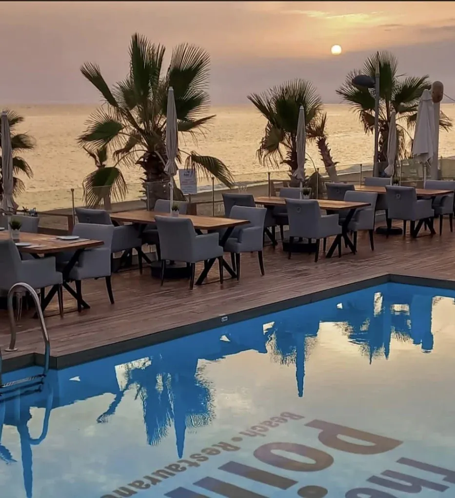 Mesas para cenar junto a la piscina con palmeras y el mar al atardecer en Marbella