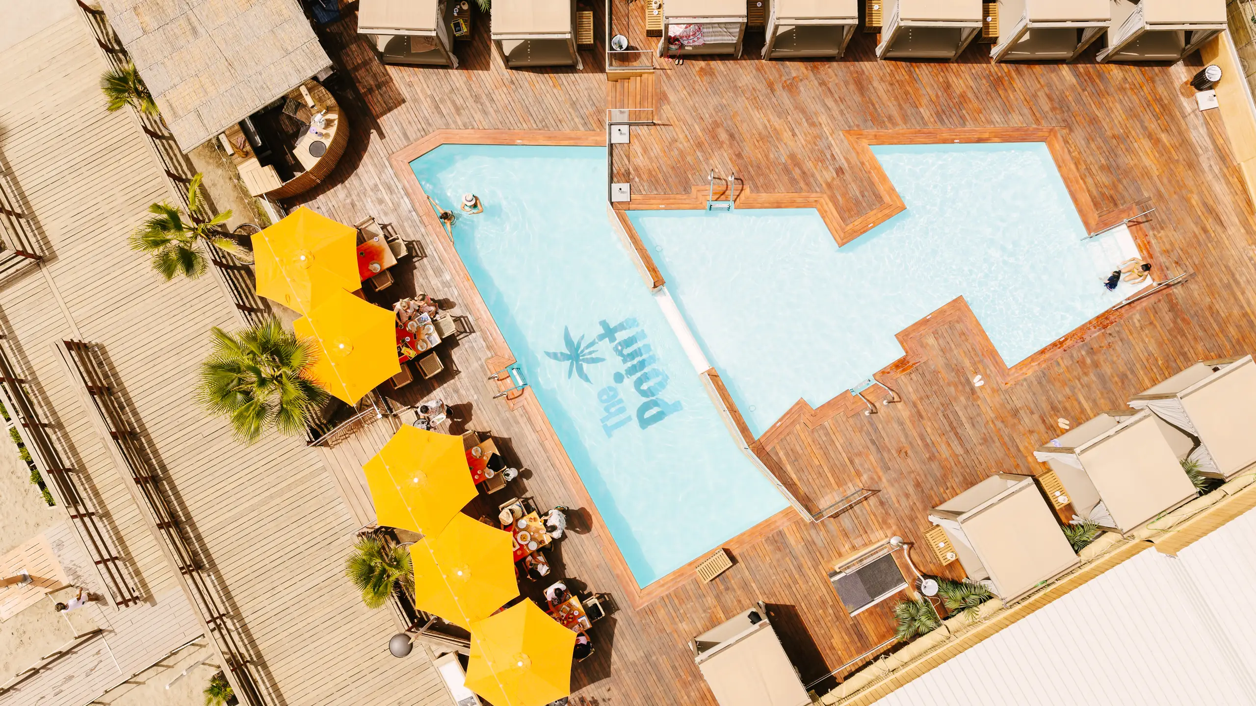 Piscina del beach club vista desde el aire con sombrillas amarillas en Marbella Este