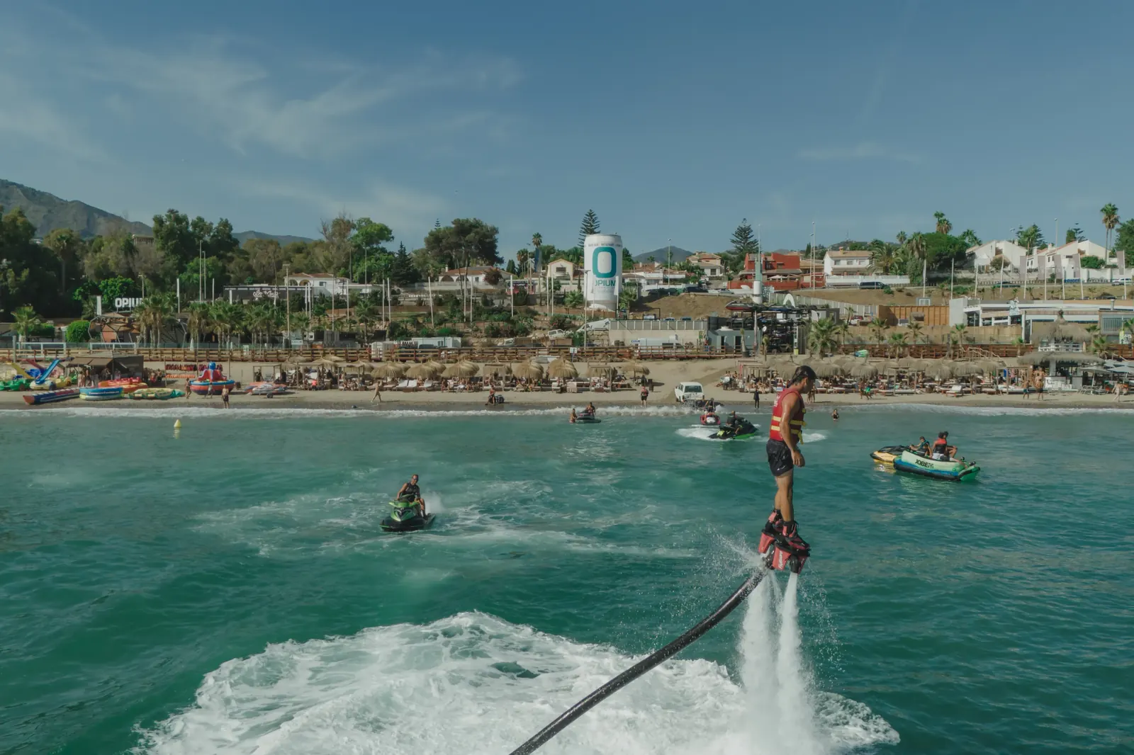 Flyboard en el mar con la playa y el beach club The Point Marbella al fondo, actividad de team building