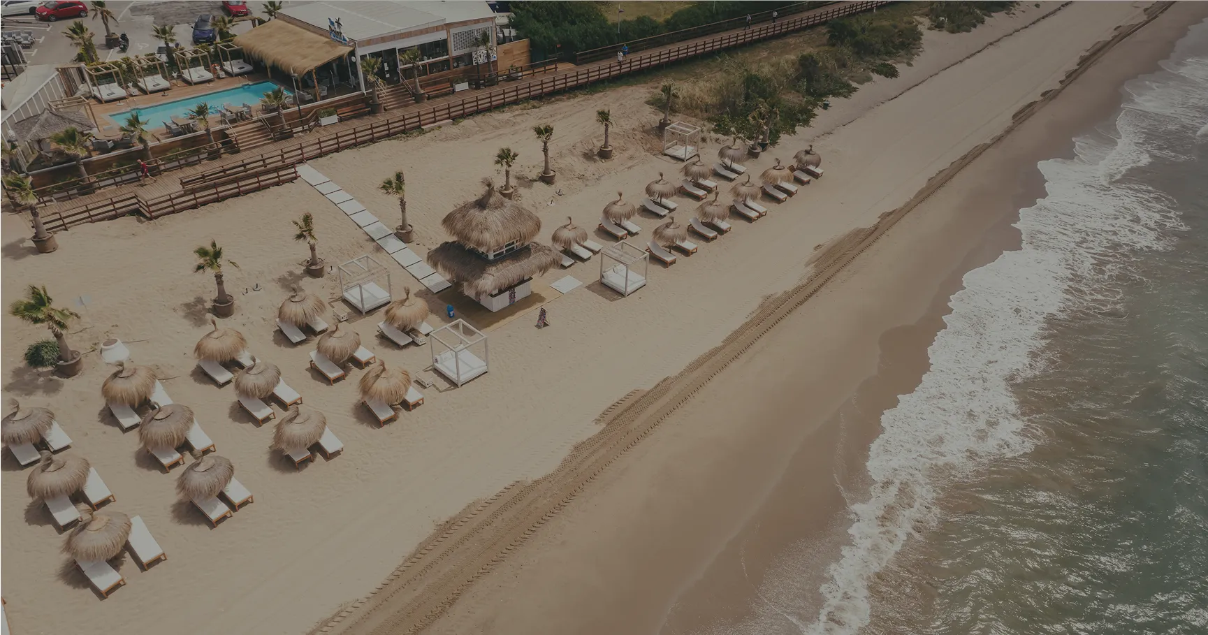 Vista aérea de The Point Marbella con cabañas, sombrillas de paja y arena dorada junto al Mediterráneo